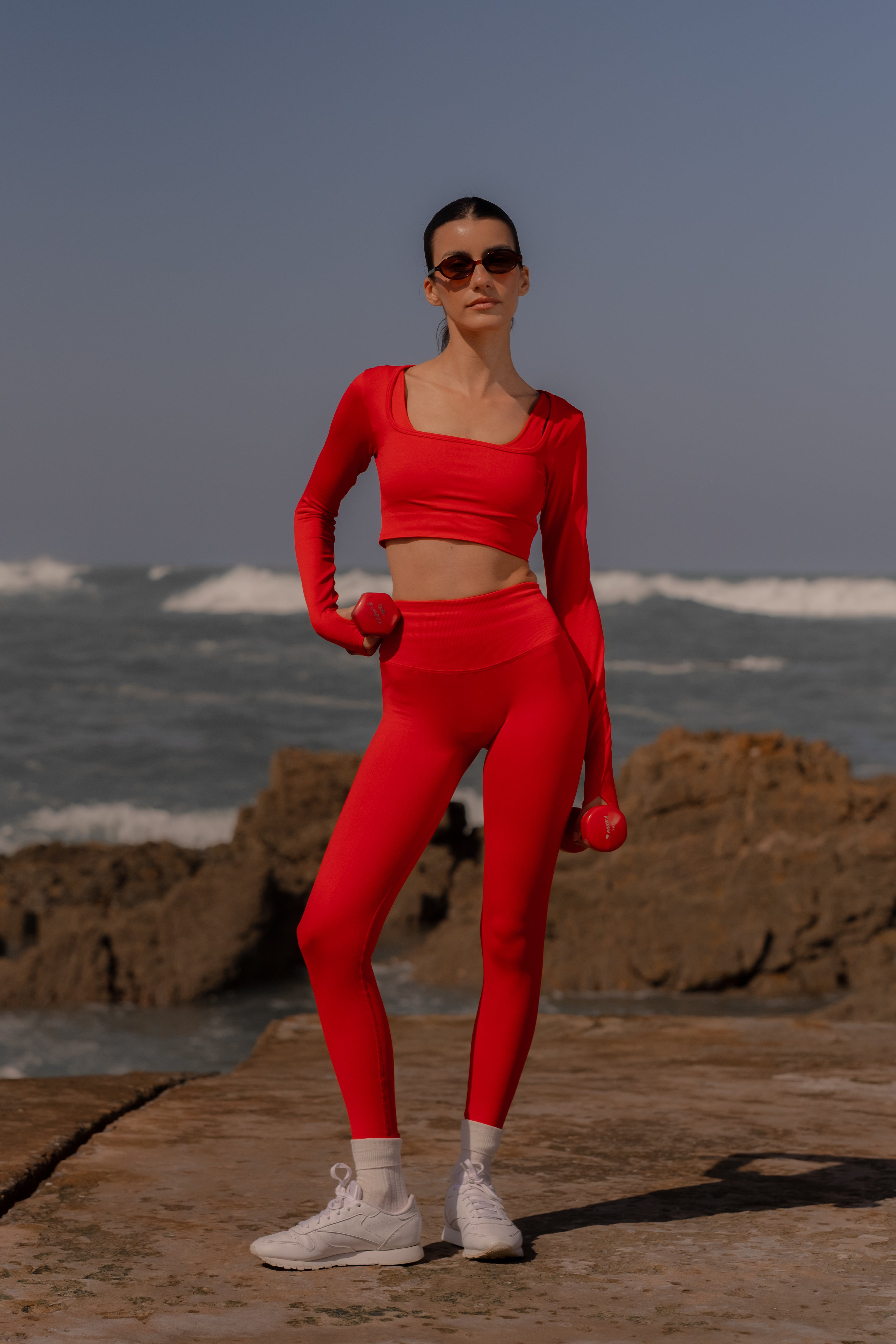 Woman in red athletic wear standing on a rocky beach with ocean waves in the background