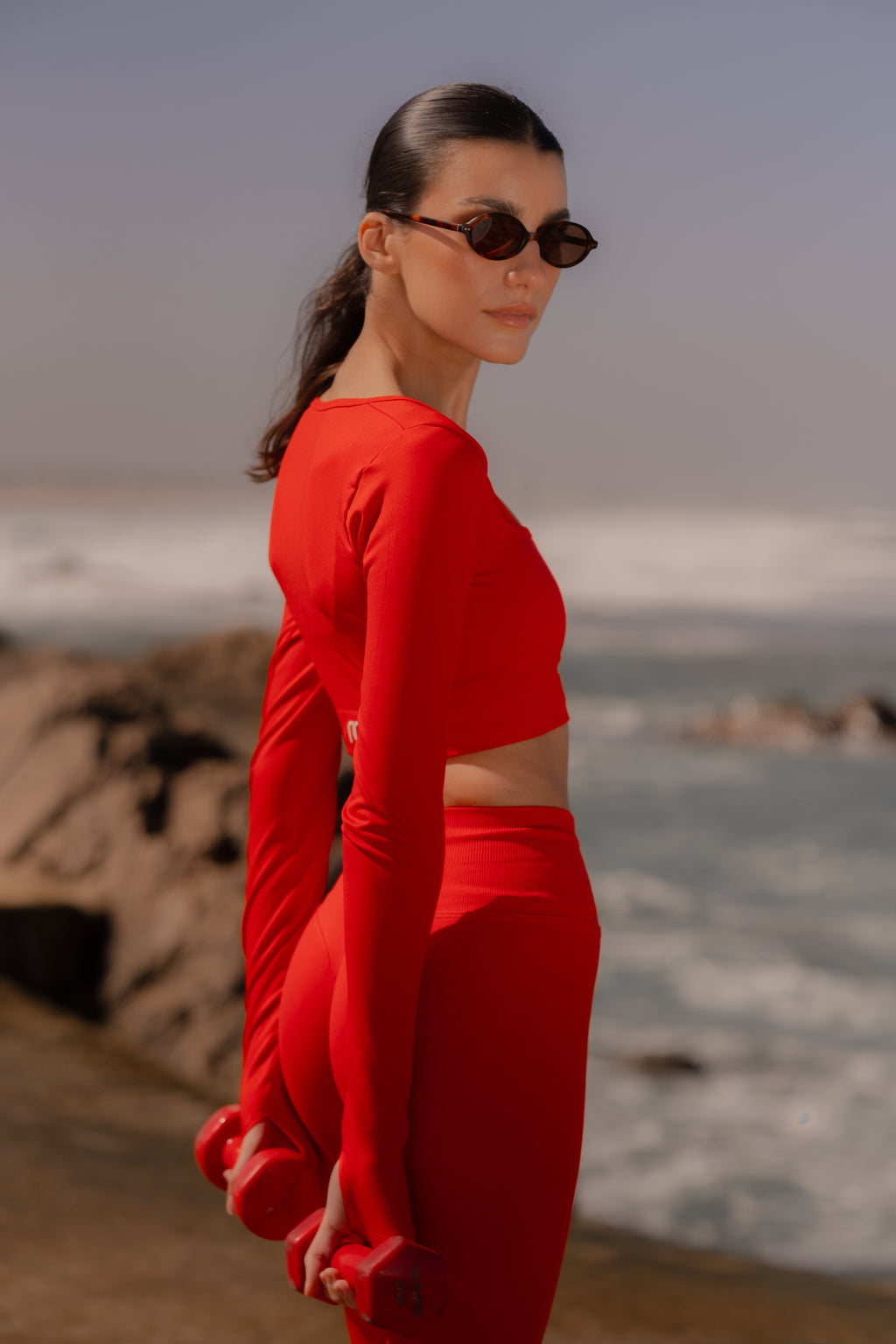 Woman in a red outfit standing on a beach with ocean and rocks in the background