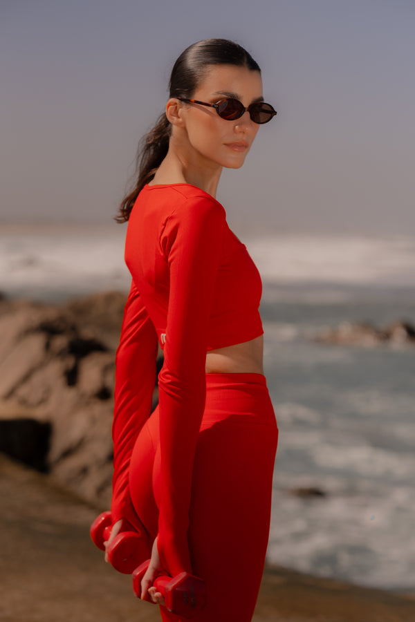 Woman in a red outfit standing on a beach with ocean and rocks in the background