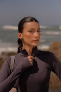 Woman in a purple outfit standing on a rocky beach with ocean waves in the background
